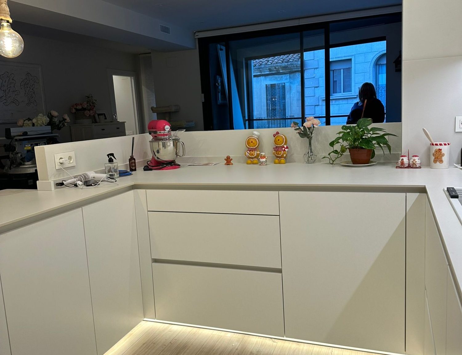 Cocina moderna con muebles blancos, una planta y decoración colorida en la encimera.